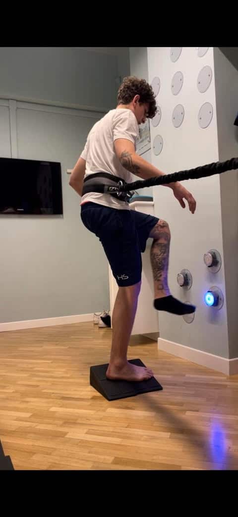 persona con una gamba tatuata in equilibrio su una piattaforma, che tiene una corda attaccata a un muro.