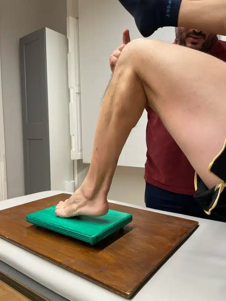 la gamba di una persona sollevata su una piattaforma verde con l'assistenza di un'altra persona, in quello che sembra essere un ambiente di terapia fisica incentrato sullo sport, che sottolinea la riabilitazione sportiva.