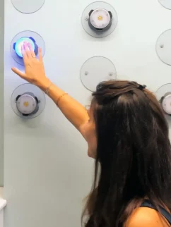 una donna interagisce con un pannello luminoso in un centro di terapia fisica. un logo sul muro recita 