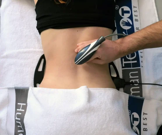 una persona è sdraiata a faccia in giù con un dispositivo portatile applicato alla parte bassa della schiena durante un trattamento. asciugamani con la scritta 