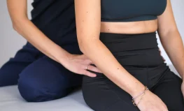 una persona vestita di nero riceve fisioterapia o un massaggio alla parte bassa della schiena da un'altra persona che indossa un vestito blu scuro.